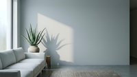 Minimalist interior with gray sofa, potted succulent plant, and natural sunlight casting shadows on blank wall, suitable for home decor and design projects.