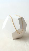 Gold chain necklace displayed on white geometric stone stand. Delicate link chain in warm metallic tone, perfect for jewelry retail, e-commerce, and fashion marketing.