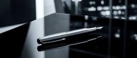 Sleek black stylus pen resting on reflective dark surface with blurred tech equipment background, suitable for digital design and technology concepts.