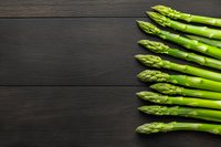 Fresh green asparagus spears arranged on dark wooden background with copy space for healthy cooking and nutrition concepts.