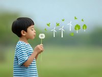 Asian boy in striped shirt blowing dandelion with green energy concept illustrations of wind turbines, trees, and birds representing renewable energy and environmental conservation.