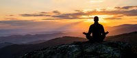 Person meditating on mountain peak at golden sunset with layered hills and dramatic sky creating peaceful spiritual atmosphere for wellness content.