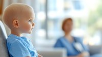 Young cancer patient in blue shirt sitting in hospital room with medical staff in background, representing pediatric oncology care and childhood illness support.