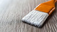 Clean white synthetic bristles on orange handle paintbrush macro shot against wooden surface, showing fine detailed brush fibers in soft focus for home improvement projects.