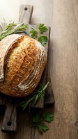 Freshly baked artisan sourdough bread loaf on rustic wooden cutting board with herbs, homemade bakery concept for culinary blogs and restaurant menus.