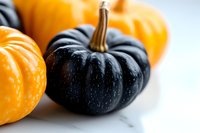 Orange and black mini pumpkins on white marble background create striking seasonal contrast, perfect for autumn decor and Halloween designs.