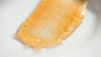 Amber-colored gel or resin substance with water droplets on white surface, suitable for cosmetics, skincare, or scientific product photography.