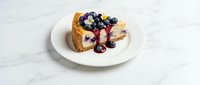 Slice of blueberry cheesecake on white plate with fresh berries, creamy dessert for bakery menu, restaurant photography, food styling concept.
