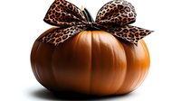 Orange pumpkin decorated with large leopard print bow on white background, seasonal autumn decor combining traditional harvest with modern animal print style.