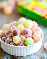 Colorful sugar-coated gummy candies in white ceramic bowl on rustic blue wooden table. Sweet round jellies in assorted fruit flavors with crystalline coating.