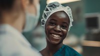Young African American female medical professional in scrubs and surgical cap smiling warmly during conversation with colleague in hospital setting. Healthcare workplace portrait.