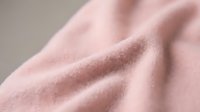 Soft pink fabric texture with gentle folds and wrinkles creating elegant shadows and highlights for fashion, textile and interior design projects.