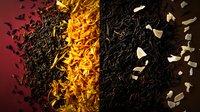 Dramatic composition of black tea leaves with golden spices and white petals scattered on dark background, creating striking contrast in warm lighting.