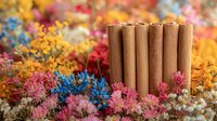 Cinnamon sticks arranged vertically surrounded by vibrant dried flowers in pink, blue, yellow and white colors creating aromatic natural composition for spa and wellness.