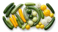 Fresh organic vegetables arranged in circular pattern on white background featuring zucchini, yellow squash, patty pan, cucumber and okra for healthy cooking.
