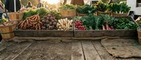 Rustic wooden crates filled with fresh organic vegetables at farmers market display, including carrots, potatoes, radishes and leafy greens for sale.