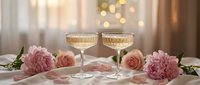 Two elegant champagne glasses filled with sparkling wine on romantic table setting with pink roses and peonies, perfect for wedding celebration or anniversary.