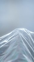Transparent plastic film with iridescent rainbow reflections creating abstract geometric shapes against soft gray background for modern design projects.