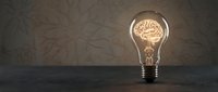 Glowing light bulb with brain filament on dark textured background representing creativity, innovation, intelligence and bright ideas for business concepts.