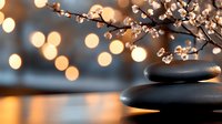 Zen spa stones with cherry blossom branch against warm bokeh lights background creating peaceful atmosphere for wellness and relaxation concept.