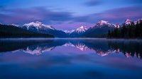 Serene mountain lake reflecting snow-capped peaks at twilight with purple and blue sky creating mirror-like surface for nature photography backgrounds.