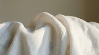 Soft white cotton fabric with gentle folds and creases creating natural textile waves and shadows for comfort and relaxation concepts.