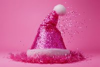 Pink glittery Santa hat with white pompom and tinsel decoration on bright pink background with scattered sparkles creating festive holiday atmosphere.