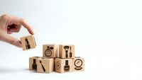 Hand placing wooden cube with restaurant icons into stack of blocks featuring dining symbols on white background for hospitality business concepts.