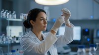Female scientist of Middle Eastern descent examining test tube in modern laboratory setting. Researcher wearing white coat and protective gloves conducting chemical or biological analysis. Professional healthcare, medical research, and scientific development concept.
