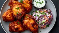 Spicy buffalo chicken wings served with creamy ranch dip and fresh coleslaw on gray plate. Crispy fried chicken pieces garnished with parsley, classic appetizer presentation.