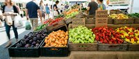 Vibrant farmers market display with fresh organic vegetables and fruits in wooden crates. Shoppers browse colorful produce stand with peppers, apples.