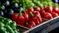 Fresh red bell peppers and vegetables in wooden box at farmers market, selective focus on bright produce with water drops for healthy eating.