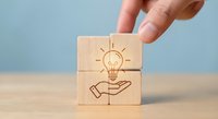 Hand placing wooden blocks with lightbulb and hand icons representing innovation, creativity and idea development for business solutions.