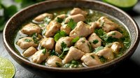 Tender chicken pieces in aromatic green curry sauce garnished with fresh herbs and lime. Served in rustic ceramic bowl, close up view of authentic Asian cuisine.