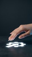 Female hand with manicured nails hovering over glowing gear icon on dark surface, representing technology, innovation, and digital interaction for web and app design.