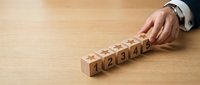 Businessman hand arranging wooden blocks with numbers 1 2 3 4 5 in sequence on desk representing step-by-step process planning and organization.