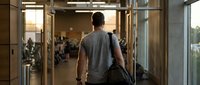 Young athletic man walking into modern gym carrying sports bag during golden hour workout session for fitness and health lifestyle motivation.