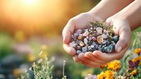 Caucasian female hands holding colorful healing crystals and stones in garden setting with orange marigold flowers and sunlit natural background.