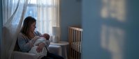 Young mother breastfeeding newborn baby in peaceful nursery room with natural window light creating intimate bonding moment for family lifestyle content.