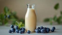 Fresh blueberry smoothie in glass bottle surrounded by ripe berries and mint leaves on neutral background, healthy breakfast concept.