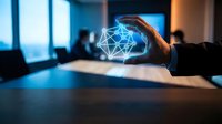 Hand holding glowing geometric network sphere in modern office workspace with colleagues in background, representing digital innovation and connectivity.