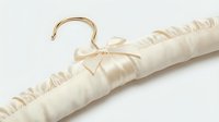 Elegant ivory satin padded clothes hanger with gold hook and bow, isolated on white background for bridal, luxury fashion, and wardrobe styling use.