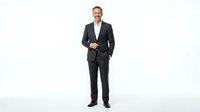 Middle-aged Caucasian male professional in formal dark suit and white dress shirt, standing confidently with hand in pocket against white background for corporate and business use.