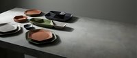 Modern minimalist table setting with terracotta plates and dark ceramic dishes on concrete surface for contemporary dining and kitchen design.