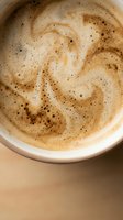Overhead view of creamy cappuccino with rich crema and cocoa powder in white ceramic cup on neutral background, suitable for café menus and beverage marketing.