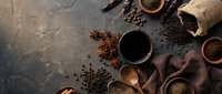 Dark roasted coffee beans scattered around black cup with aromatic spices including star anise and cinnamon sticks on textured surface for cafe branding.