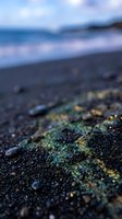 Close-up of dark volcanic black sand beach with glowing green and gold mineral particles, ocean waves softly blurred in background.