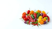 Assorted fresh bell peppers and chili peppers arranged on white background, including red, yellow, orange, and purple varieties with green stems for culinary and food styling projects.