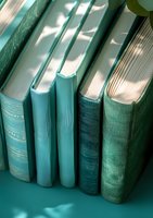 Row of vintage hardcover books in shades of turquoise and teal with natural window light casting shadows, creating atmospheric literary composition.