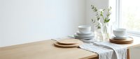 Minimalist dining table setting with white ceramic plates, bowls and eucalyptus branch in glass vase on linen runner creating serene scandinavian home decor.